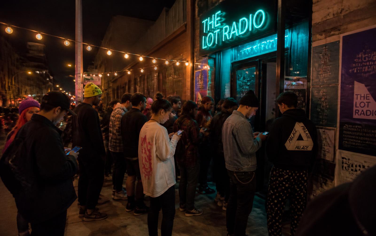 People waiting in line outside a small music venue under a glowing marquee
